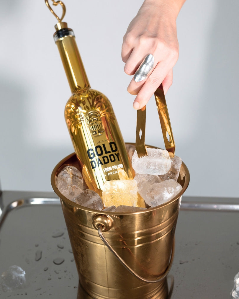 Gold Daddy Vodka bottle in an ice bucket with a hand using tongs to add ice