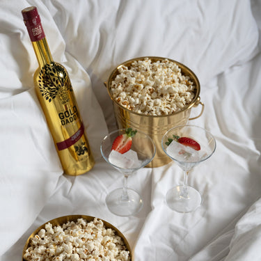 Two glasses with ice and strawberries, a popcorn bucket, and a bottle of Gold Daddy Cherry Kiss