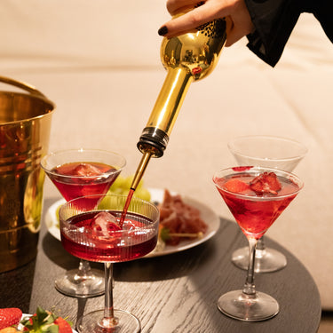 Cocktails on a table with a hand pouring Gold Daddy liqueur into a glass