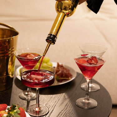 Cocktails on a table with a hand pouring Gold Daddy liqueur into a glasses