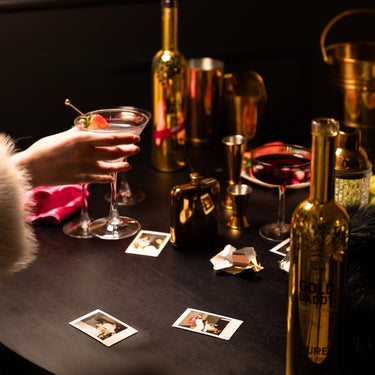 Woman’s hand in a fur coat holding a cocktail made with strawberry liqueur, over a table